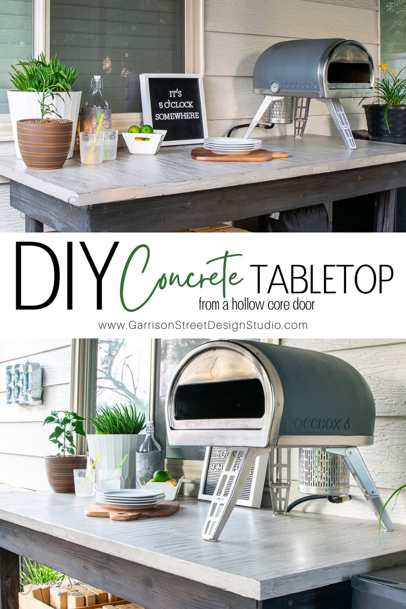 A DIY concrete outdoor table anchors the setup, topped with two modern pizza ovens. Surrounded by plants, dishes, and kitchenware, a small chalkboard cheerfully notes "It's 5 o'clock somewhere." Rustic wooden frames complete this inviting outdoor kitchen oasis.