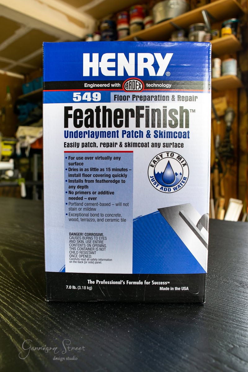 A box of Henry FeatherFinish 549 Floor Preparation & Repair product is on display. The packaging highlights its use in underlayment patching and skim coating, emphasizing easy application and strong adhesion to various surfaces. Weight: 7 lb (3.18 kg).