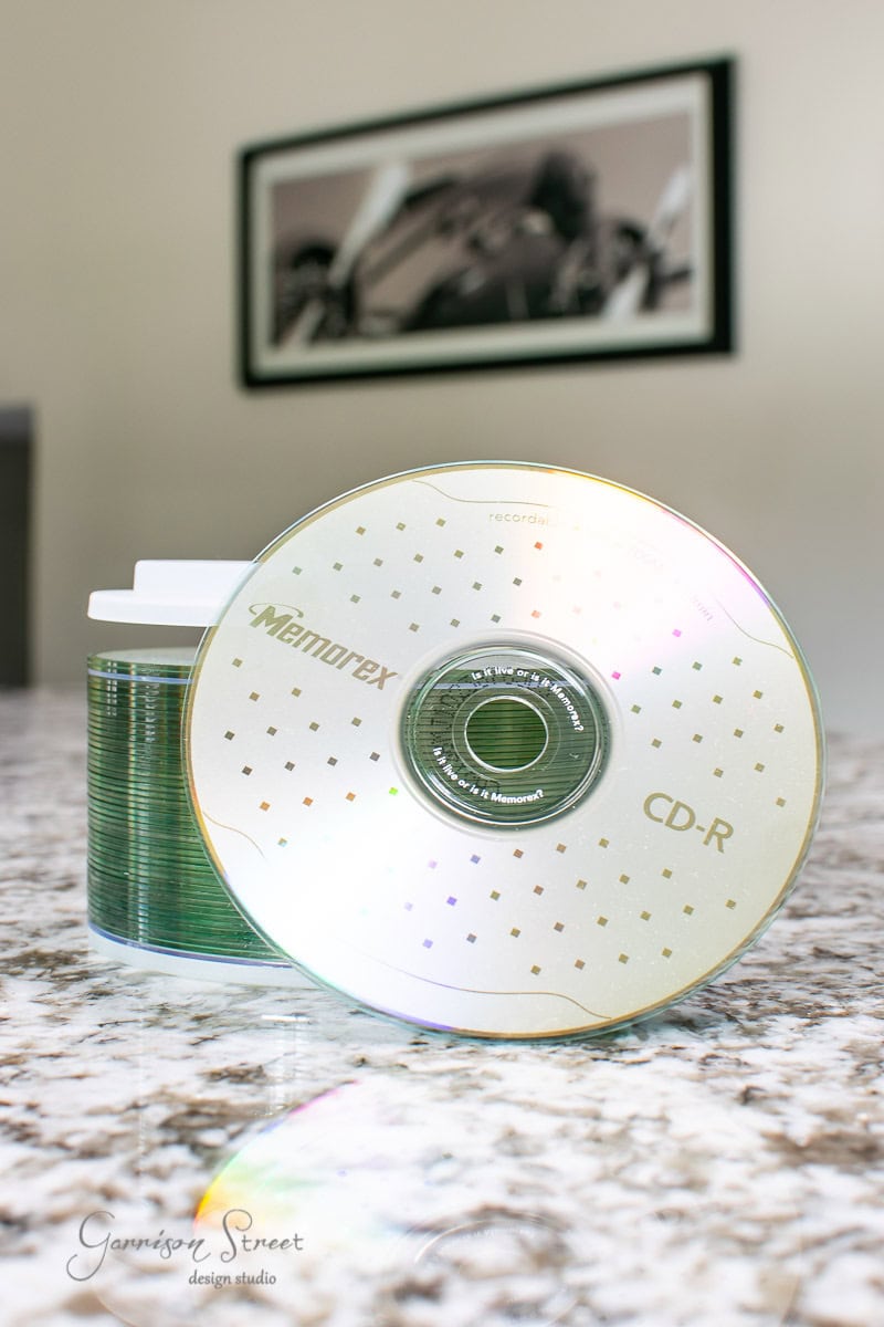 A stack of Memorex CD-Rs is partially visible, with one disc leaning against the stack on a sleek IKEA granite countertop. A blurred black and white photograph is mounted on the wall in the background.