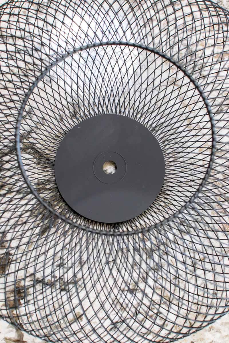 Top view of an empty, IKEA wire mesh trash bin with a circular black base, placed on a marbled floor. The mesh creates a spiral pattern as it converges towards the center.