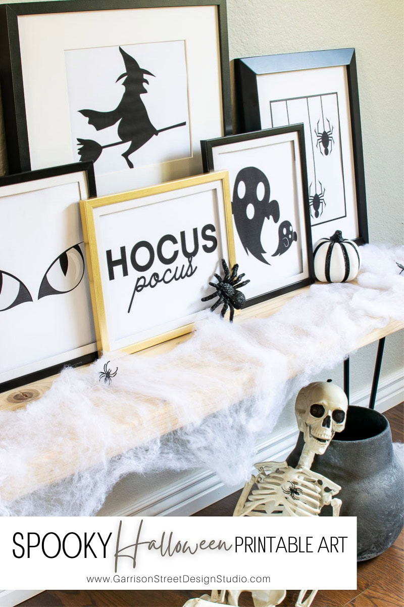 A Halloween-themed display features framed art with witch, spider, and "Hocus Pocus" graphics. A skeleton sits below, surrounded by cobwebs and spiders, adding a spooky touch.