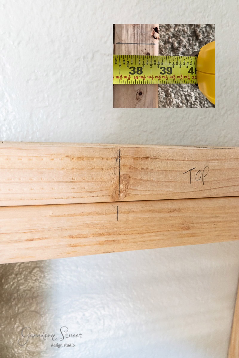 Close-up of wooden beams with pencil marks labeled "TOP," and an inset image of a measuring tape showing 38 inches, likely part of a built-in bunk beds project. Branding text at the bottom left corner reads "Garrison Street Design Studio."