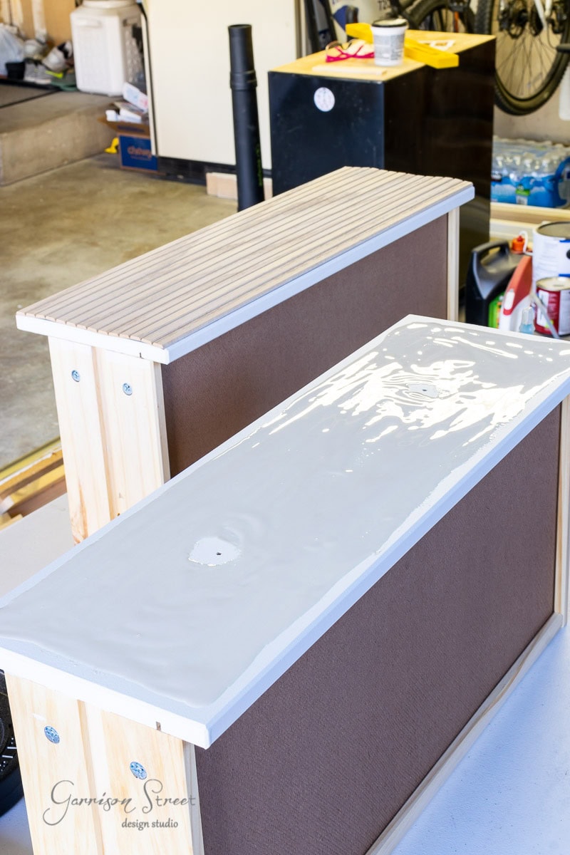 A DIY project in progress showcases a wooden tabletop coated with glossy white epoxy resin. Ripples and reflections play across its surface while various garage tools and supplies sit in the background.