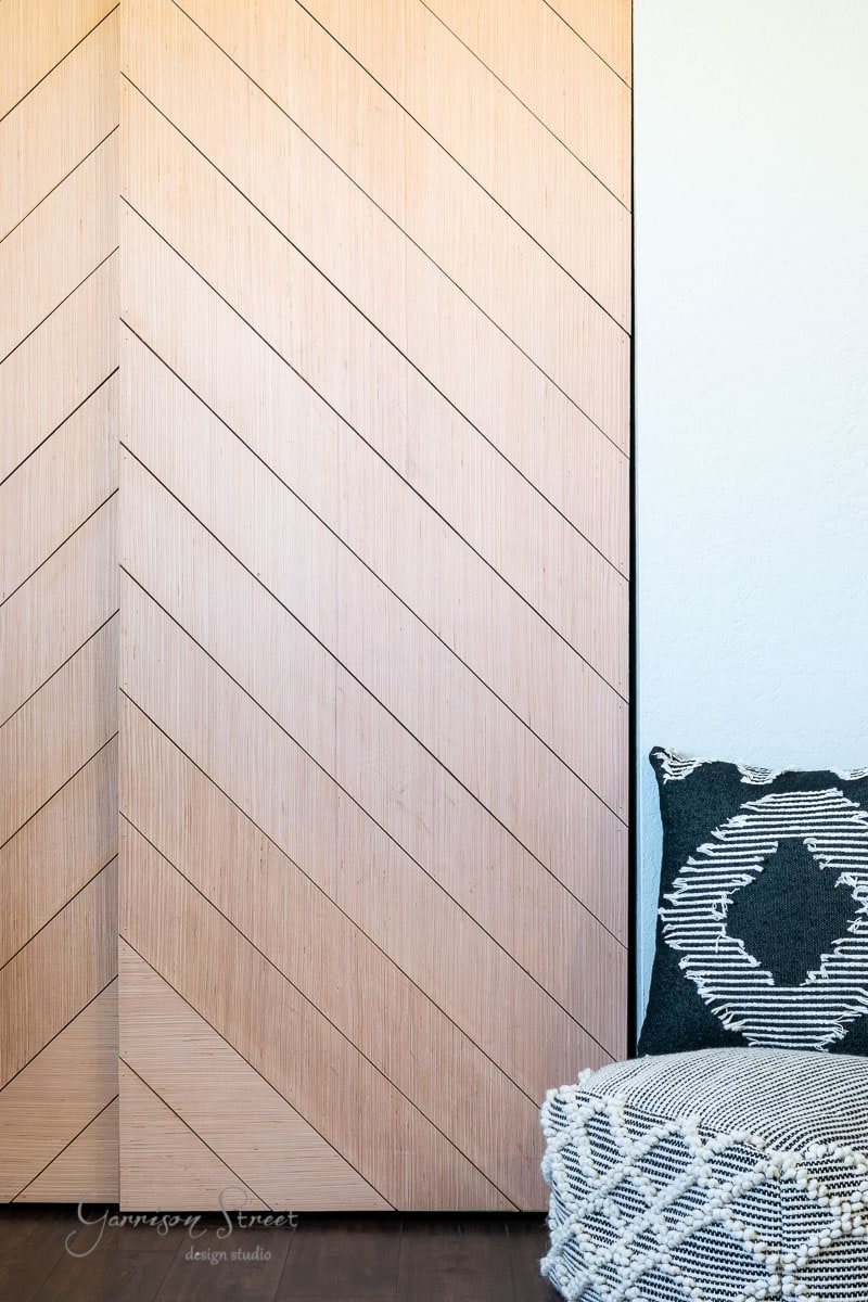 A modern wooden closet door with diagonal grooves sits beside a textured black and white cushion and blanket, creating a cozy corner with geometric patterns.