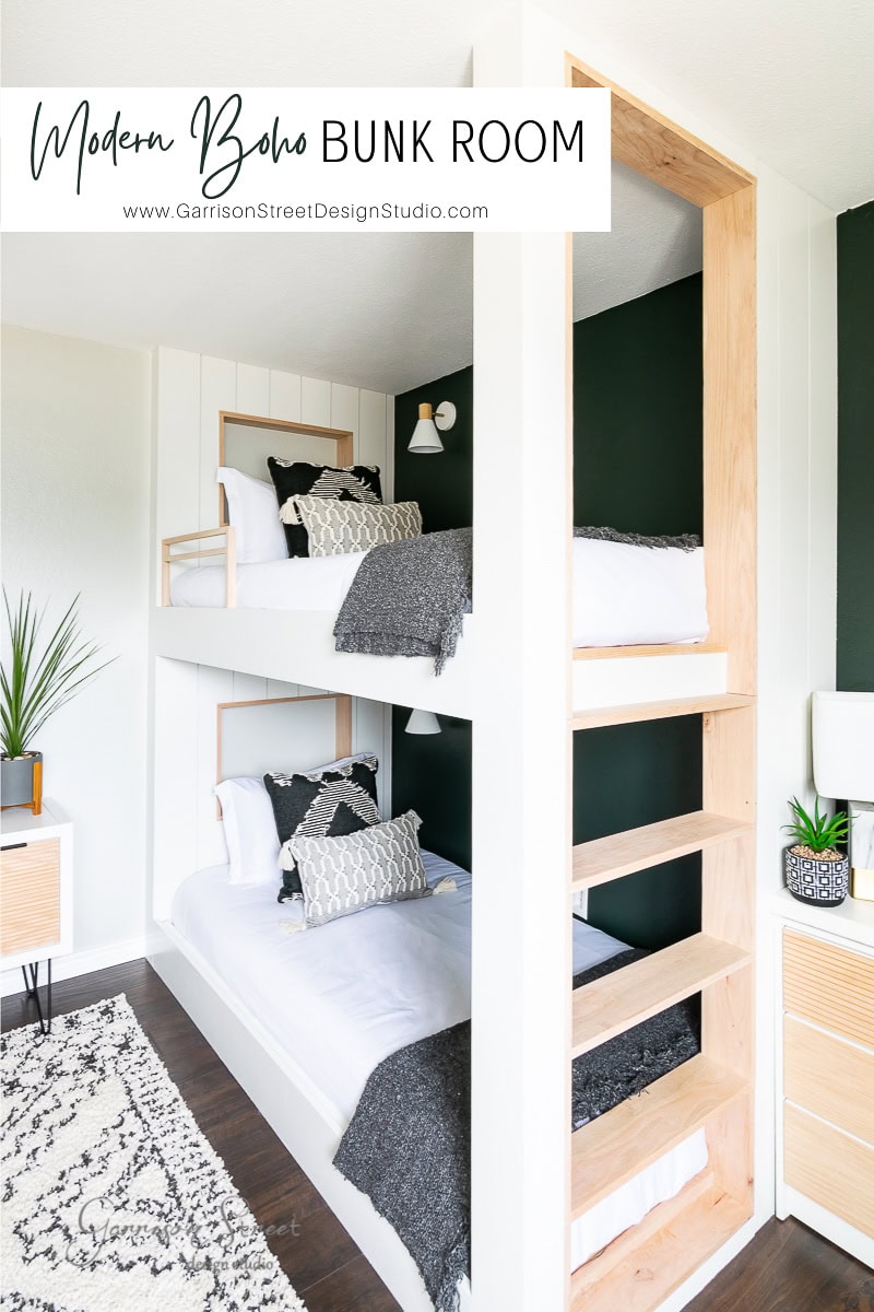 This modern boho bunk room features two bunk beds against a stylish green and white wall. The beds are dressed in white linens, gray blankets, and patterned pillows. A natural wood ladder and shelves add warmth, while a woven rug and sleek decor enhance the minimalistic charm.
