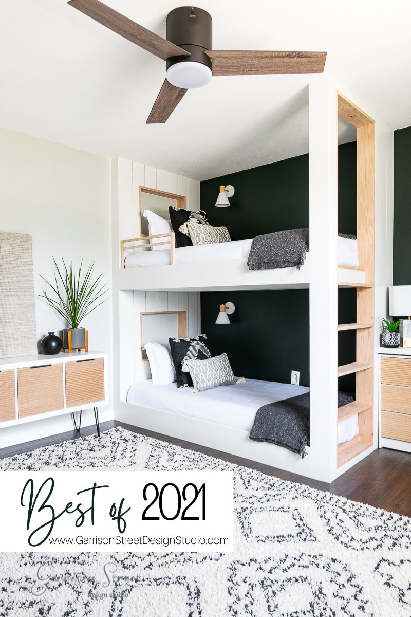 Modern bedroom with a bunk bed featuring dark green accent walls, wooden detailing, and white bedding. A ceiling fan and stylish decorations enhance the cozy, contemporary look. Text overlay reads "Best of 2021" at www.GarrisonStreetDesignStudio.com.