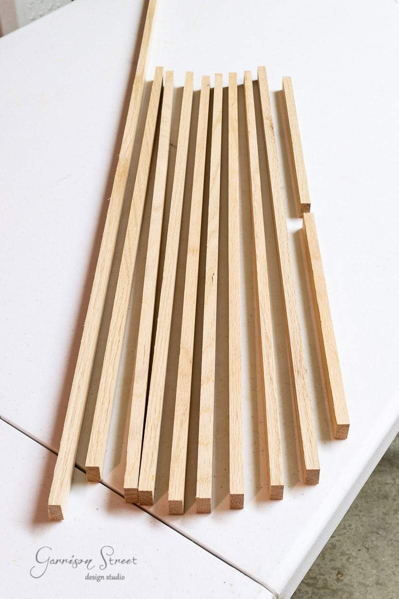 A series of light wooden strips, reminiscent of miniature scrap wood Christmas trees, are neatly arranged on a white surface, fanned out slightly. The wood has a smooth, natural finish.