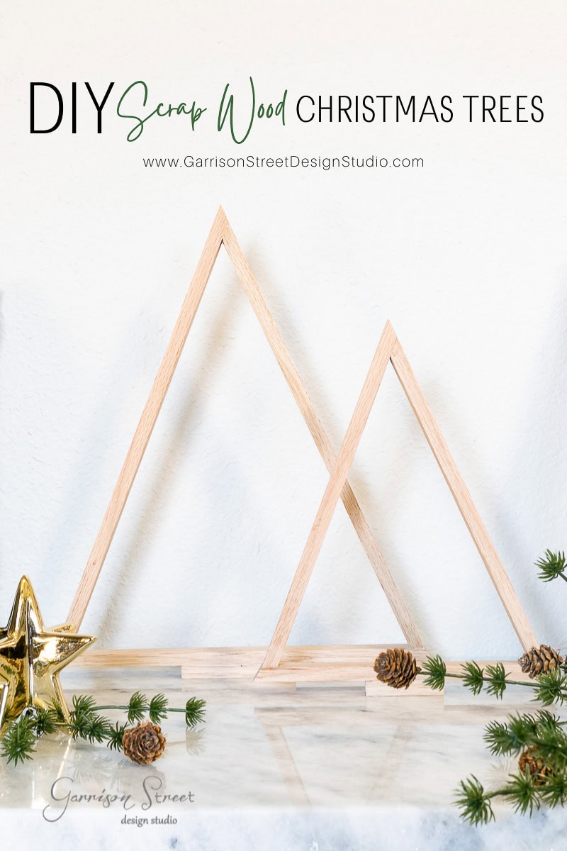 Wooden Christmas tree frames crafted from scrap wood form a triangular shape on a marble surface, surrounded by small pine branches, pine cones, and a gold star. The words "DIY Scrap Wood Christmas Trees" are displayed prominently at the top.