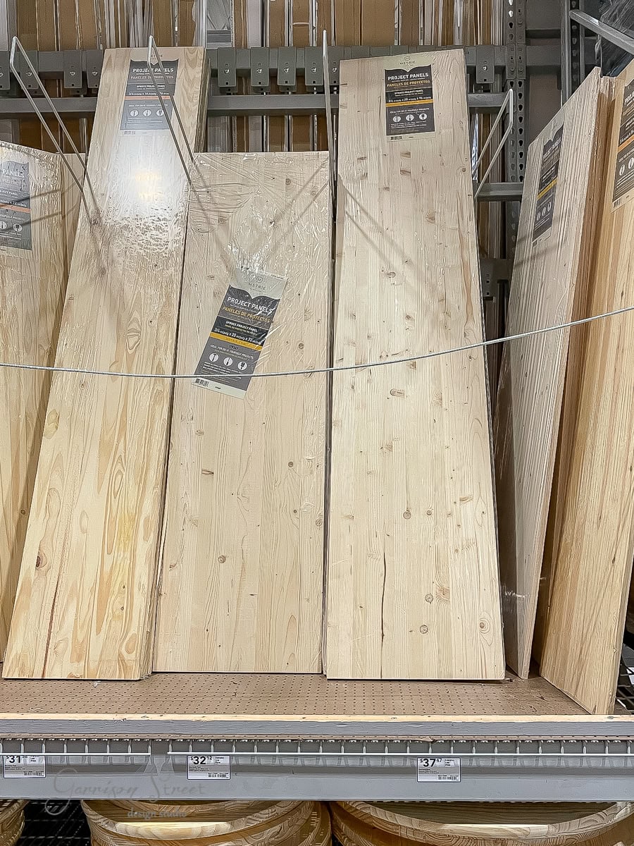 A stack of wooden planks displayed vertically on a store shelf, each labeled for easy identification. Perfect for DIY projects like crafting a custom bed frame, this section of the hardware store is surrounded by other construction materials.
