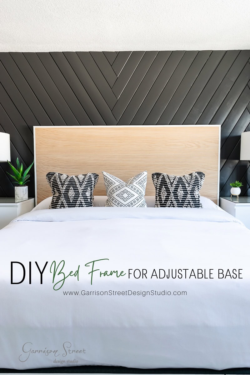 A modern bedroom highlights a chic DIY bed frame with a wooden headboard and adjustable base, adorned with black and white patterned pillows. A striking black chevron-patterned wall, cozy white blankets, and two lush plants on bedside tables complete the harmonious look.