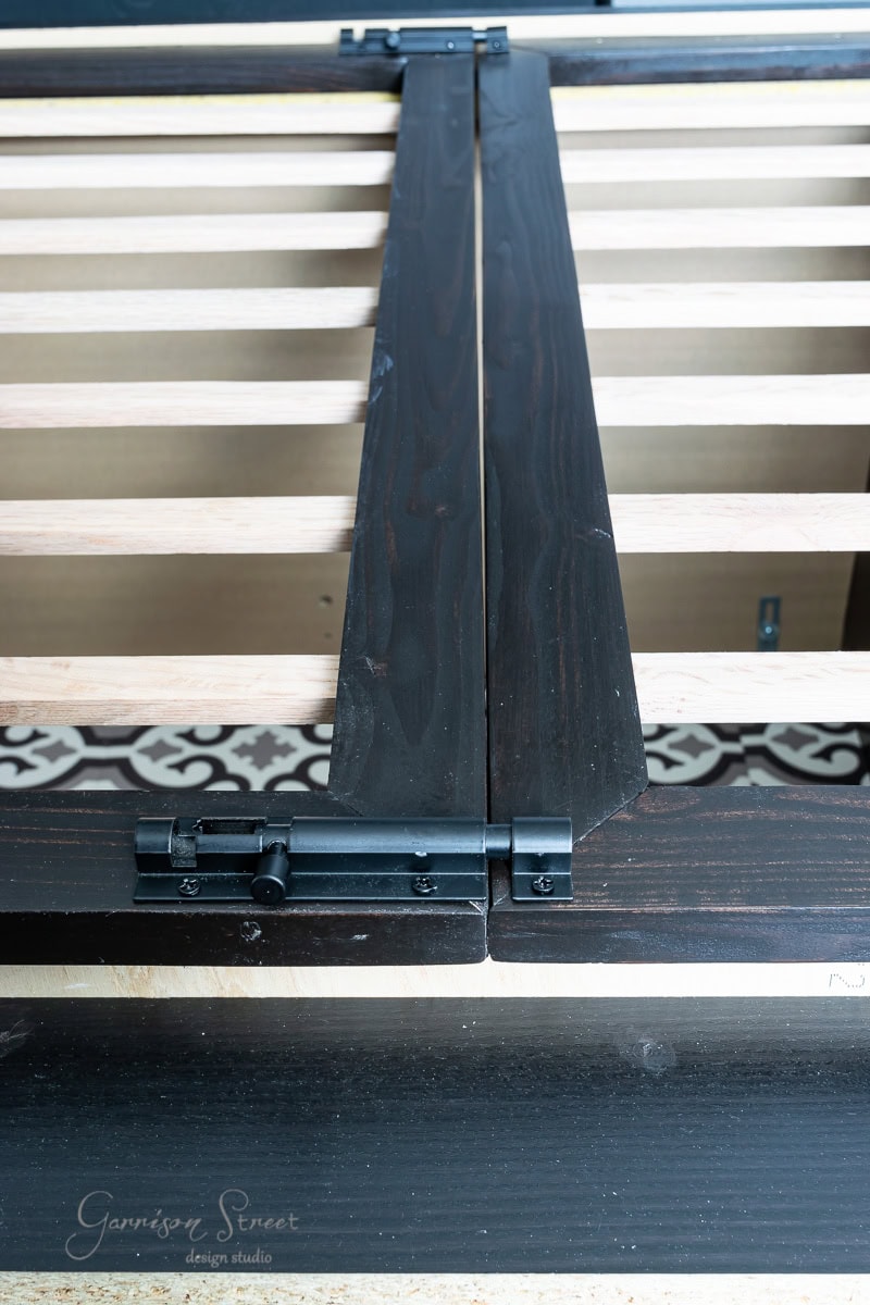 Close-up of a black sliding barn door rail against a wooden slatted surface, reminiscent of an IKEA Malm finish. The door features metal hardware, and beneath, a patterned floor is partly visible—a sneak peek into stylish home interior design.