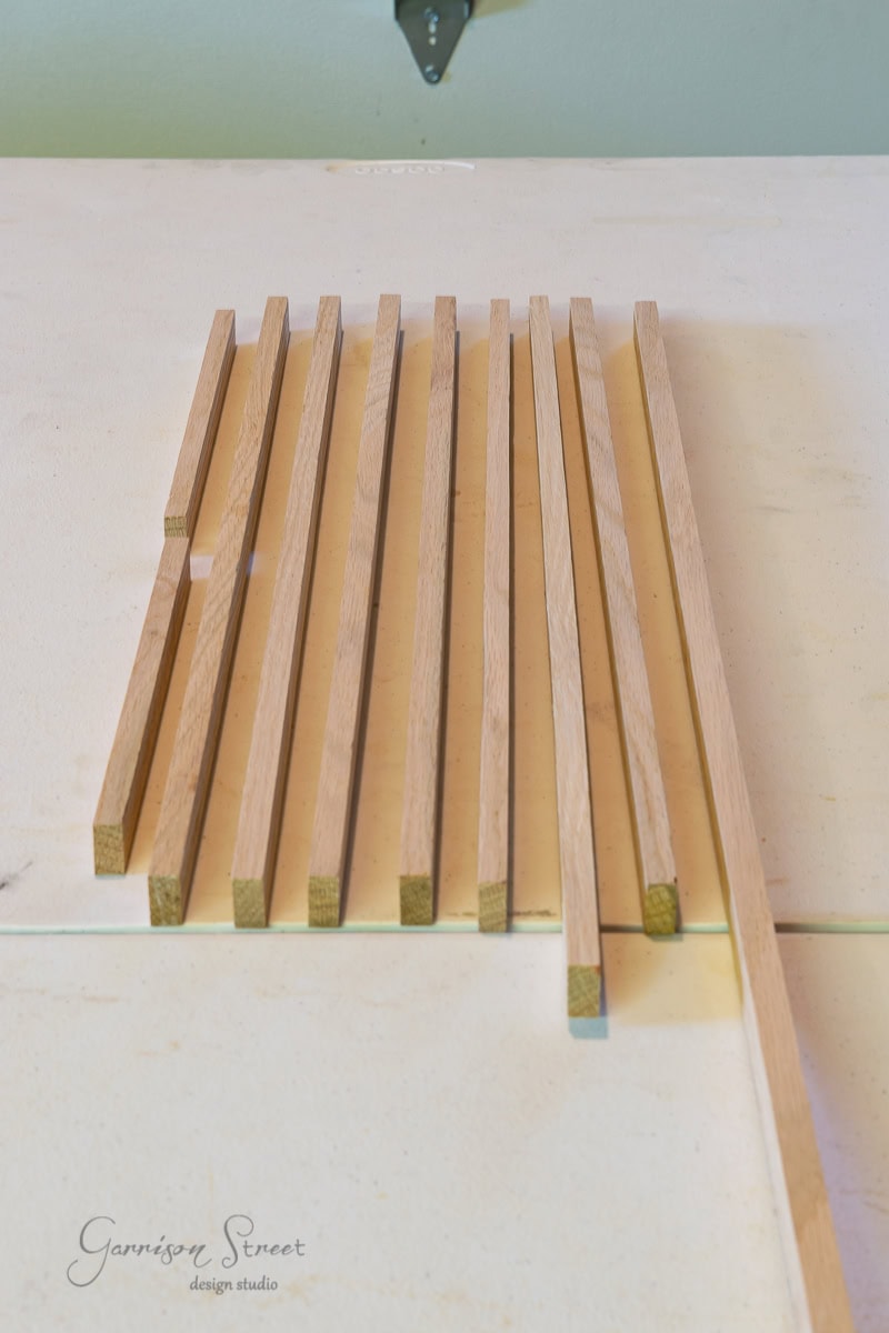 Several wooden slats, reminiscent of the minimalist design of an IKEA Malm piece, lie parallel on a light-colored surface. The slats are of equal length and neatly aligned next to each other.