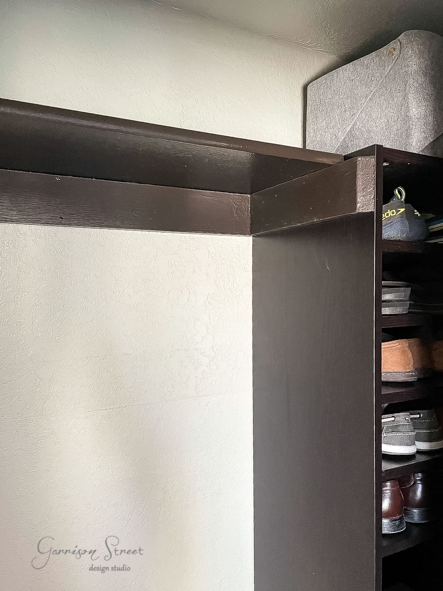 A partially open wooden closet resembling an IKEA Pax features a shoe rack on the right filled with various shoes. A gray storage box sits on the top shelf, and the white interior keeps things bright. "Garrison Street design studio" is elegantly displayed on the wall of this reach-in closet.