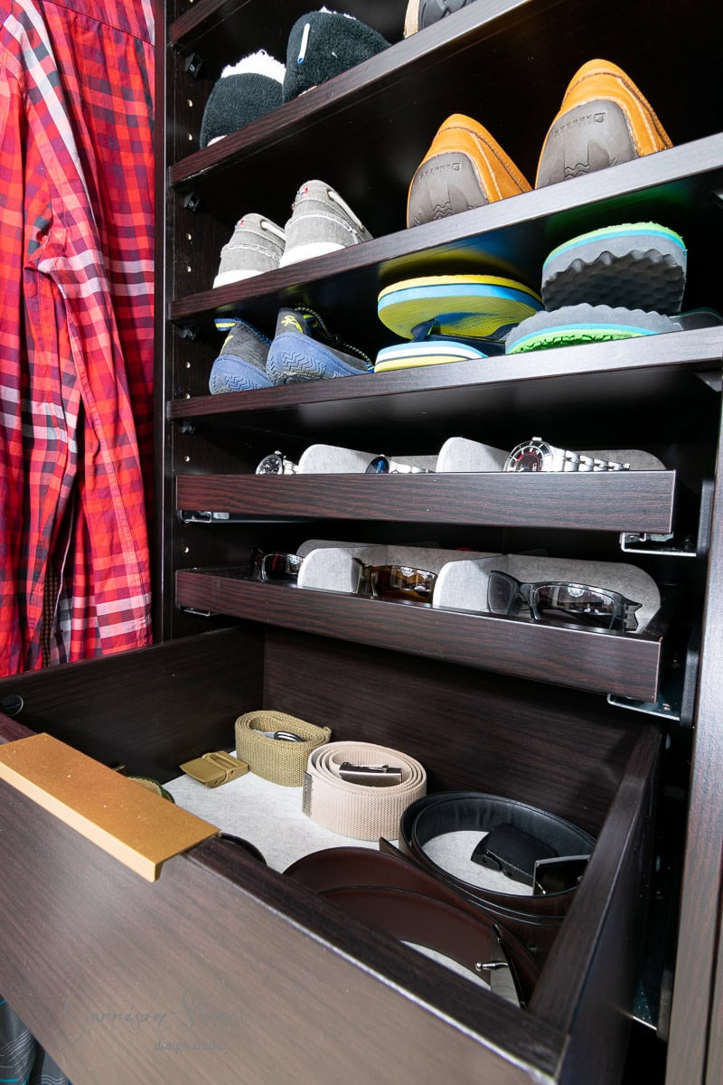 A neatly organized reach-in closet features IKEA Pax shelves holding various shoes, a rack of sunglasses, and a drawer containing belts. A red plaid shirt hangs stylishly on the side.