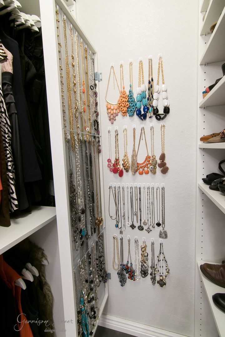 A cleverly designed closet includes a wall-mounted jewelry organizer showcasing an array of necklaces in diverse colors and styles, like beaded and chain designs that look expensive. On the left, clothing is neatly arranged, while shelves with shoes line the right—perfect for those seeking IKEA hacks.