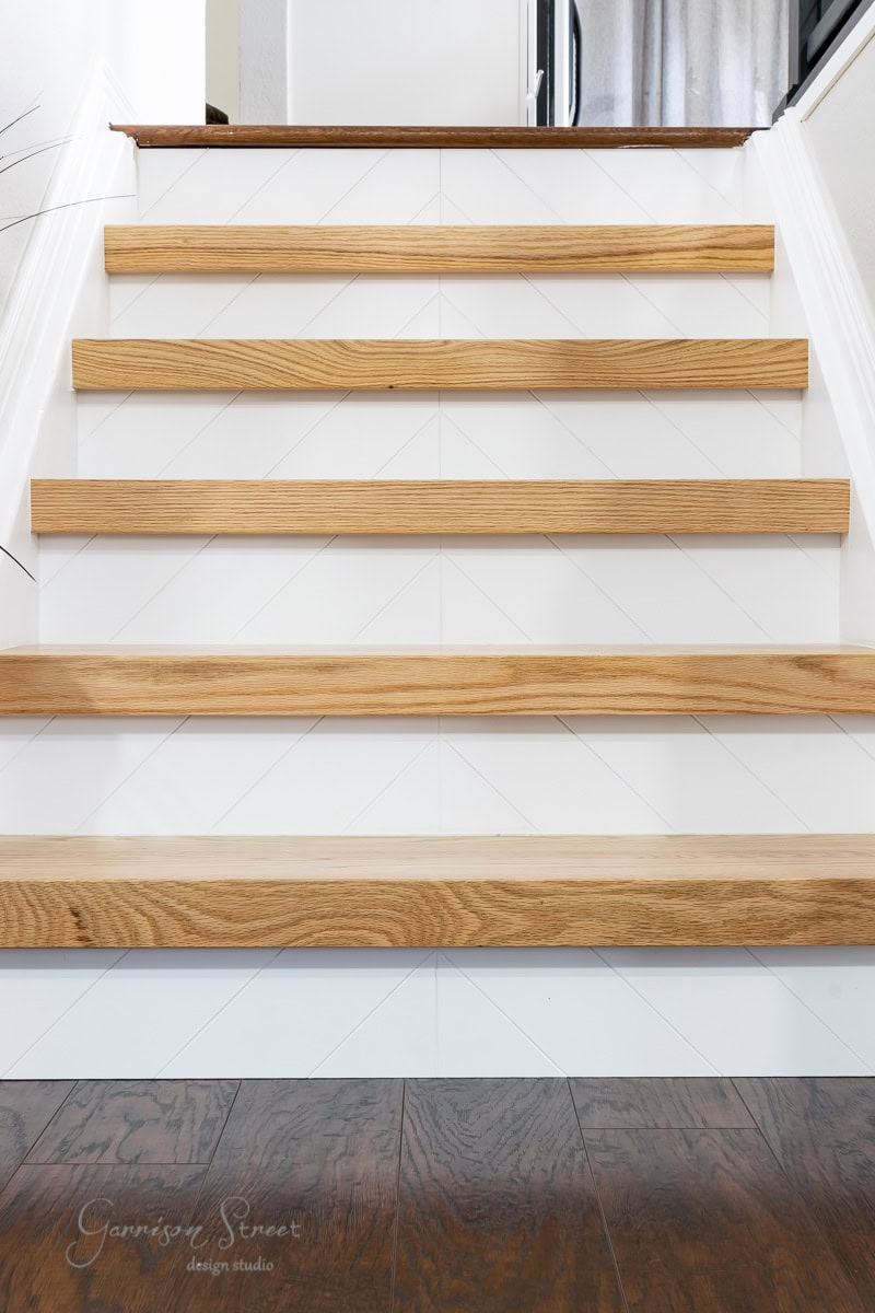 A staircase with six wooden steps leading upwards, featuring light brown treads and white risers with a subtle chevron pattern. The dark wood floor at the base contrasts beautifully with the stairs.