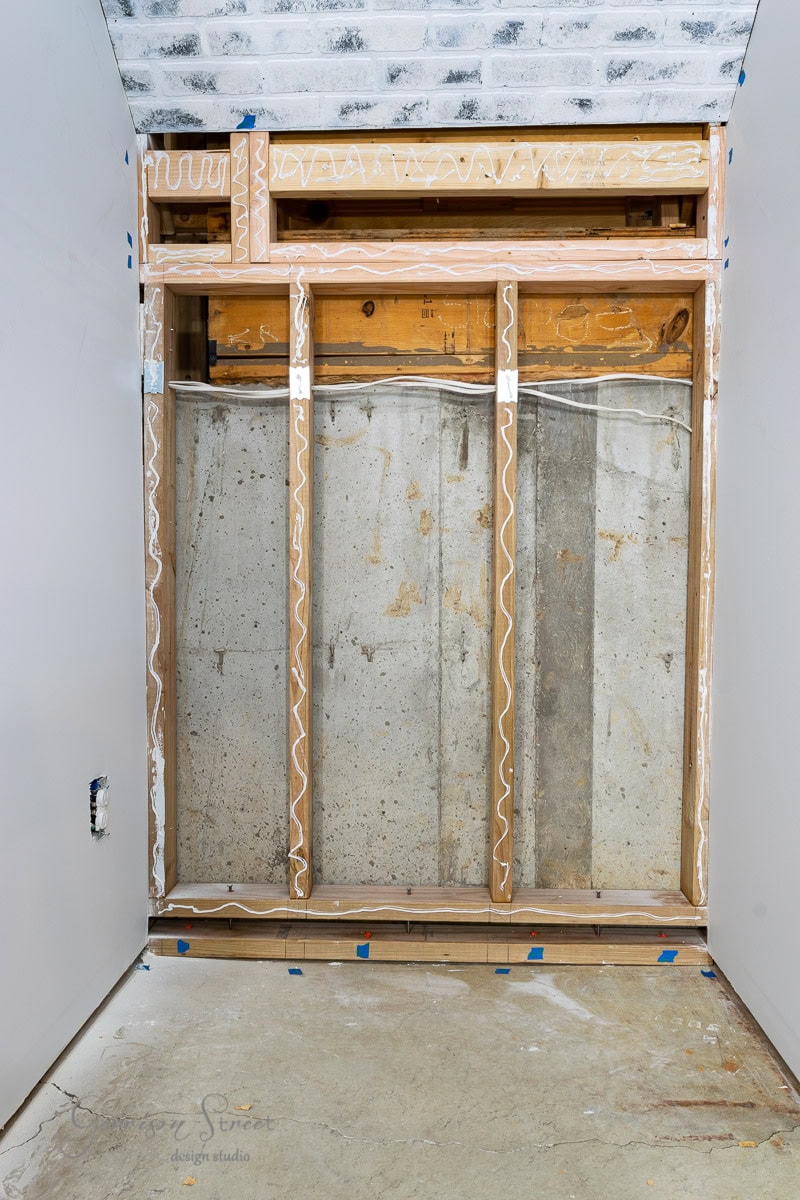 The image showcases a basement wall with exposed wooden studs and visible electrical wiring, offering alternative ideas to traditional drywall finishes. The floor and ceiling remain unfinished, highlighting the ongoing construction project.