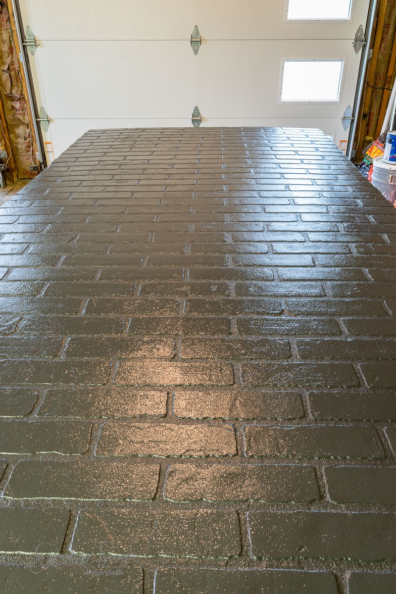 A glossy finish on the wet brick wall in the garage offers a unique alternative to standard basement wall ideas not drywall. Natural light filters through small door windows, enhancing the shiny texture of the bricks, while supplies and tools are partially visible around the area.
