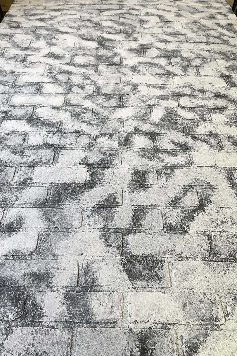 The image presents a pattern of gray brick pavers with a textured surface, arranged in a herringbone style. This design, inspired by basement wall ideas not using drywall, features a whitewashed look with varied tones creating a weathered appearance.
