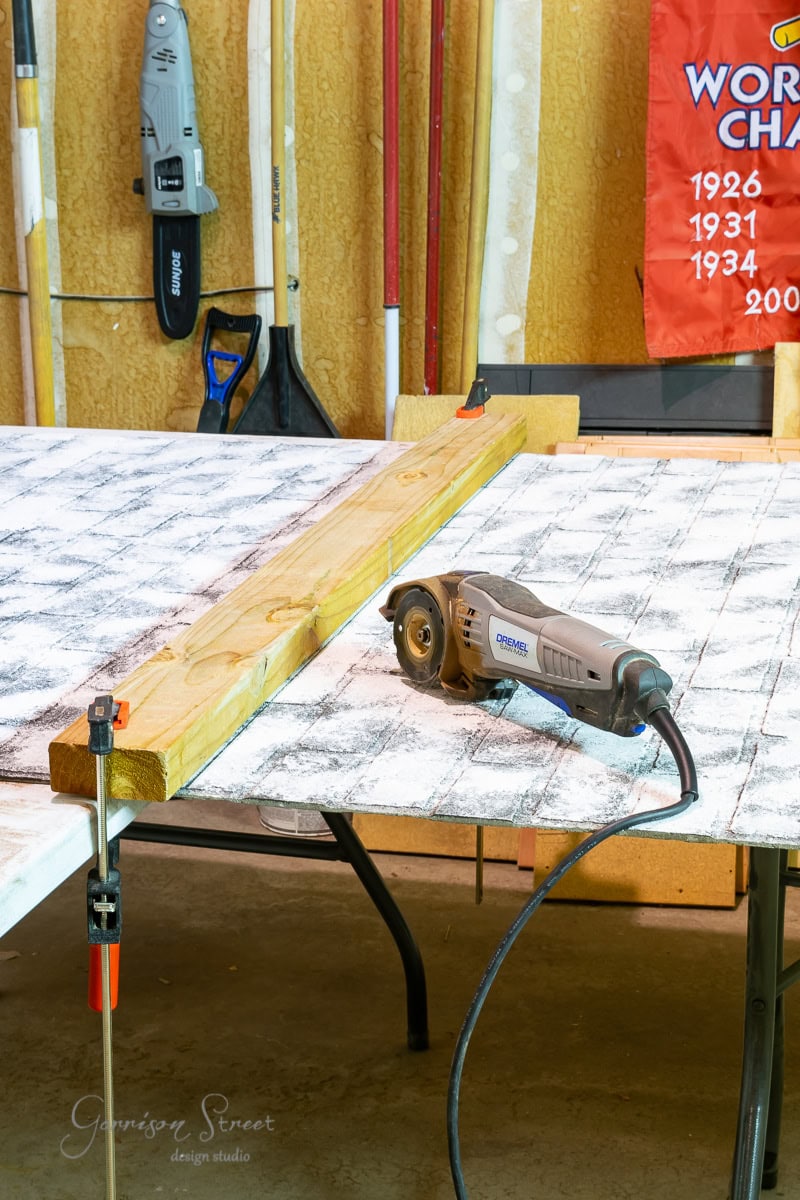 A woodworking setup in the basement features a circular saw on a table with a white and black pattern. A wooden plank is clamped to the table, surrounded by an array of tools on the wall. A red banner displaying different years adds character, showcasing unique basement wall ideas, not drywall.