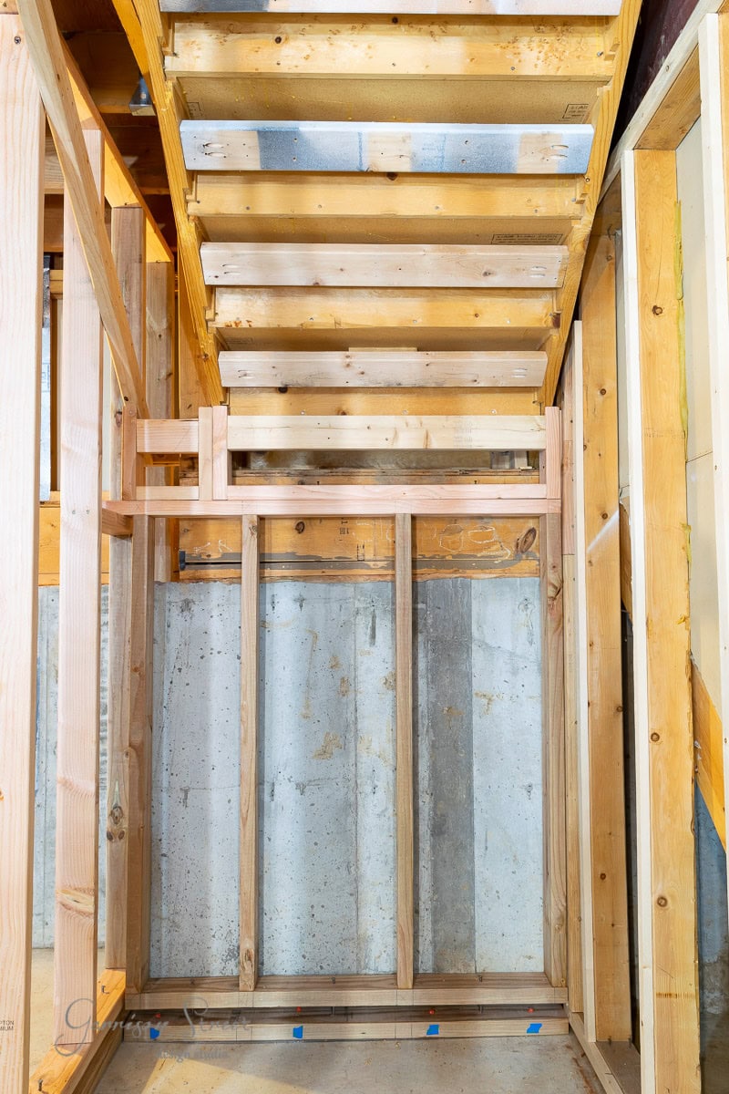 The view captures a wooden staircase under construction, set amid concrete walls and exposed framing. Offering insight into how to frame basement walls, the image showcases the structural elements beneath the stairs in this partially finished building interior.
