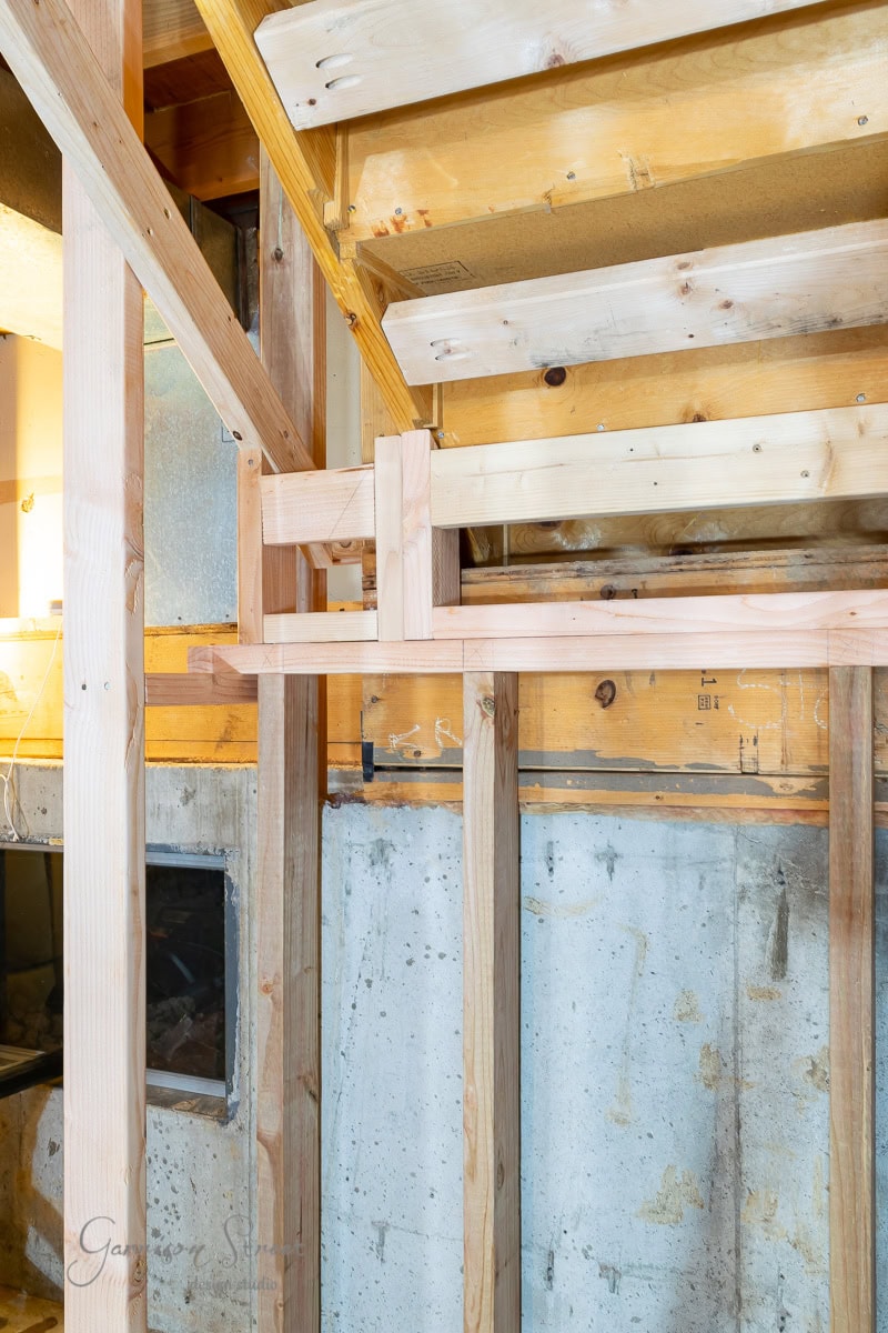 Wooden framing inside a house under construction, showcasing raw lumber beams and studs, much like learning how to frame basement walls. The image highlights the structure against a concrete foundation wall with some visible electrical wiring.