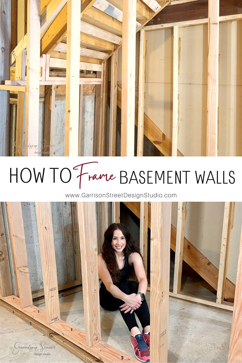 A woman sits on the floor of a partially constructed basement with wooden frame walls, smiling in her black outfit and red shoes. Discover more about "how to frame basement walls" at Garrison Street Design Studio.
