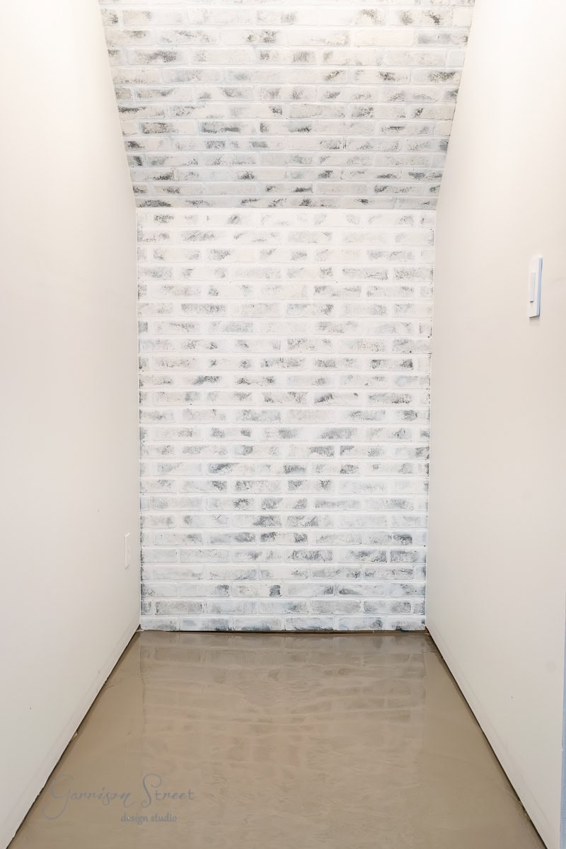A narrow hallway with a glossy beige floor and whitewashed brick wall at the end. The white side walls and ceiling create a minimalist and clean space.