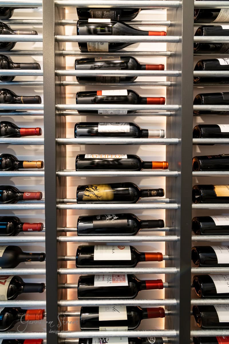 A vertical wine rack brimming with red wines, each bottle displayed horizontally and evenly spaced, labels proudly outward. Set against a light background, showcasing a diverse palette of labels and hues.