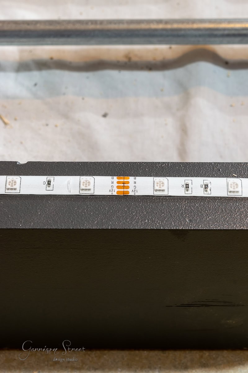 Close-up of a black LED strip with several LED lights spaced evenly apart, mounted on a flat surface. A faint watermark of a design studio is visible in the bottom corner, perfect for illuminating your latest DIY project, like building your own wine rack.
