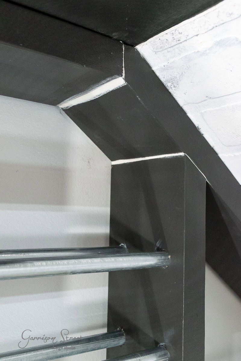 The image captures a close-up of a modern, geometric metal staircase in gray and black, showcasing sharp angles and sleek metal rods. It's reminiscent of the precision needed for a DIY wine rack project. A signature graces the lower left corner, adding an artistic touch.