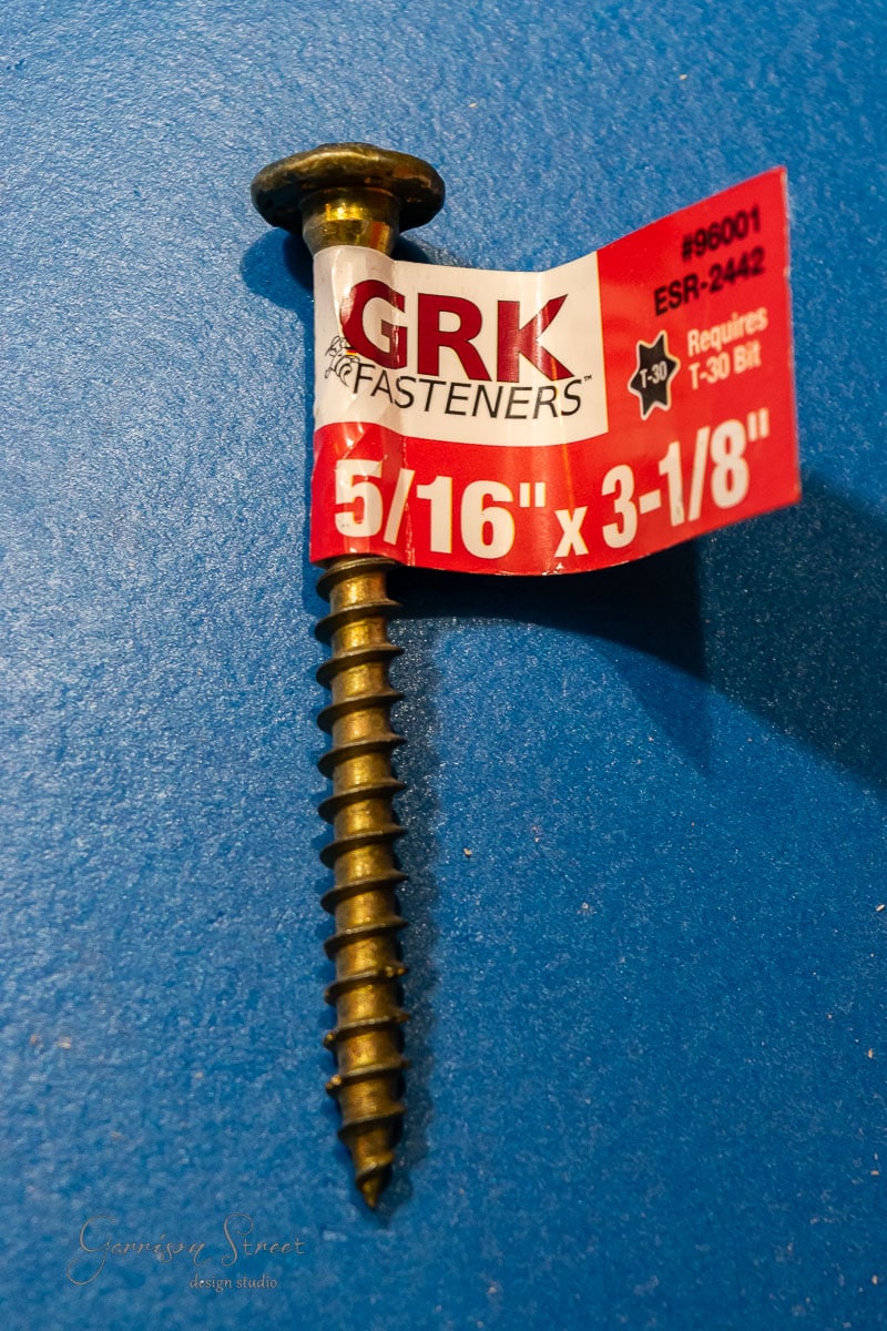A single GRK Fasteners screw sits on a blue surface, its label displaying "5/16" x 3-1/8"", "#96001, ESR-2442, Requires T-30 Bit". Ideal for those learning how to build a DIY wine rack.