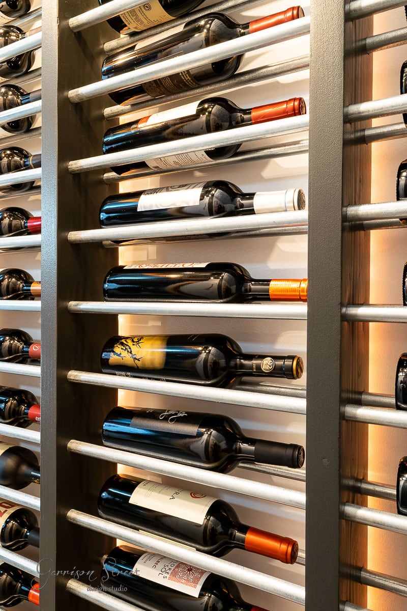 A wall-mounted wine rack filled with assorted wine bottles elegantly showcases your collection. The horizontal metal bars securely hold the bottles, while distinctive labels and colorful caps add visual appeal. Perfect for those interested in how to build a DIY wine rack.