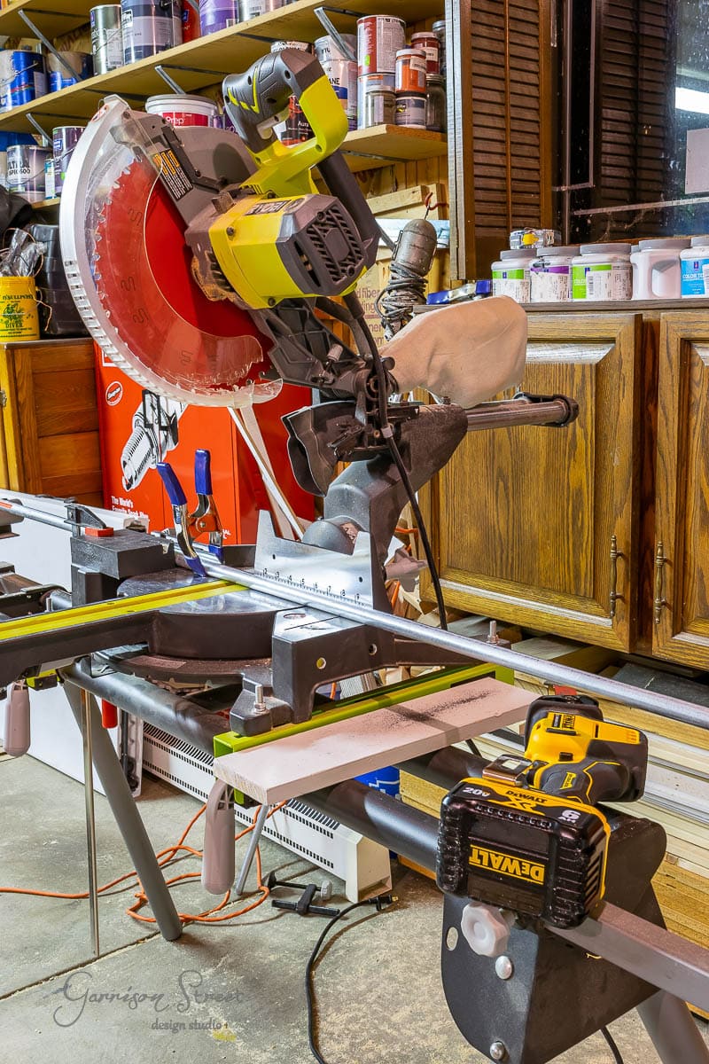 The workshop is set for creativity, with a mounted miter saw featuring a bright red blade ready to bring projects to life. Amidst various tools, equipment, and wooden cabinets lies the secret to your next creation: how to build a DIY wine rack with precision and ease.