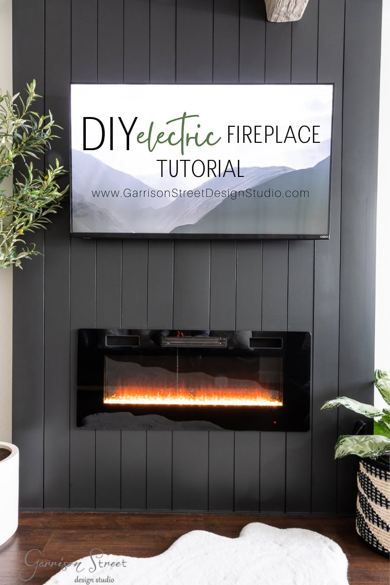 A modern living room with a black shiplap wall showcases a sleek electric fireplace beneath a mounted TV, which highlights the "DIY Electric Fireplace and TV Wall Tutorial." A green plant adds a touch of nature to the cozy space.