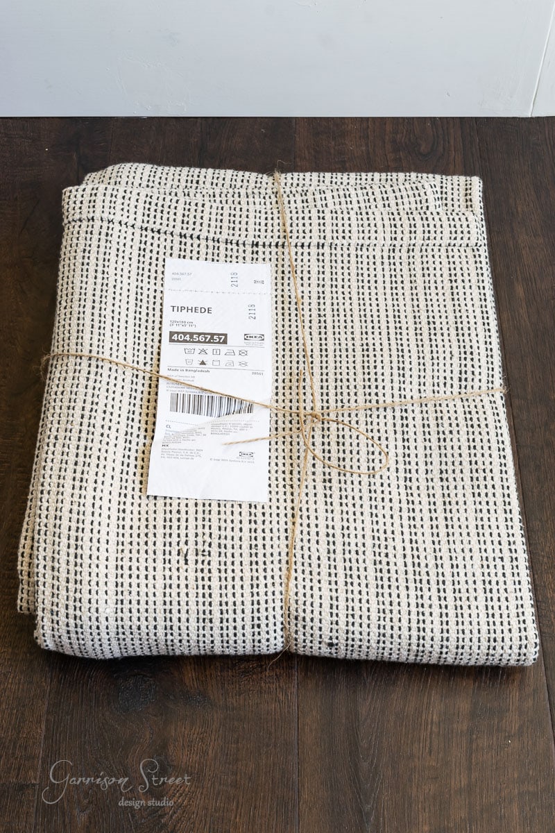 Folded white and black speckled curtain, perfect for DIY fabric wall art, tied with string and placed on a dark wooden floor. A label on the fabric reads "TIPHEDE" along with product details.