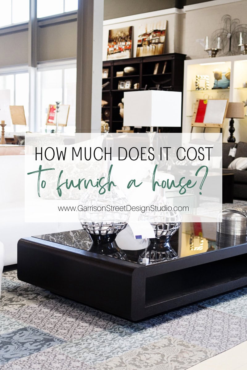 A modern furniture store interior showcases a variety of lamps, tables, and decor. A sign intriguingly asks, "How much to furnish a 4 bedroom house?" with the website "www.GarrisonStreetDesignStudio.com" inviting curious minds to explore more.