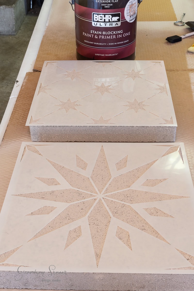 Two stone tiles are laid on a surface, each featuring a star-shaped pattern. A can of Behr Ultra Stain-Blocking Paint & Primer sits behind them.