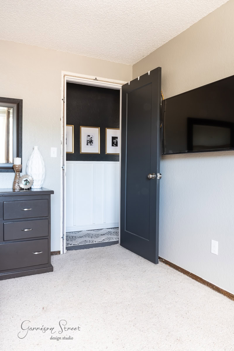 A dark dresser and mounted TV sit against light-colored walls. The open door reveals an accent wall adorned with framed photos. A light carpet and minimalist decor complete the room.