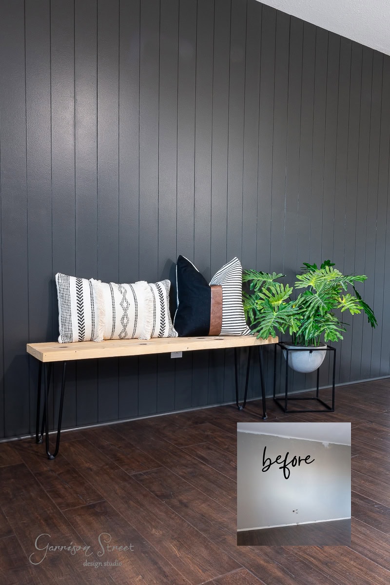 A modern interior features a wooden bench with black metal legs, decorated with assorted pillows and a potted plant. The dark shiplap accent wall contrasts with the light wood bench. An inset shows a "before" image of the same wall, bare and undecorated, highlighting the DIY transformation.