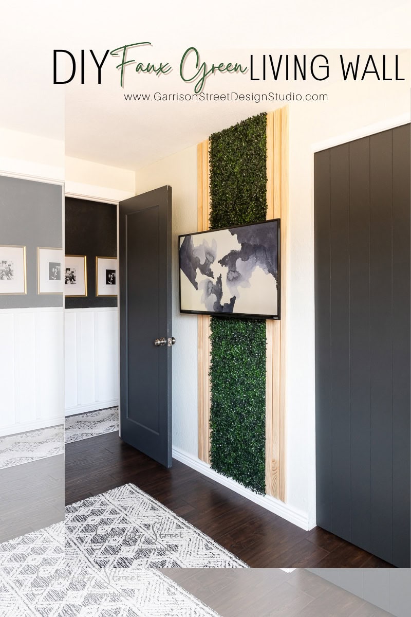 Interior room scene with a DIY faux green living wall panel, showcasing lush greenery between wood panels. A framed abstract art piece adorns it. Grey doors, wall art, and a patterned rug complete the modern look. Text reads "Green Wall DIY."