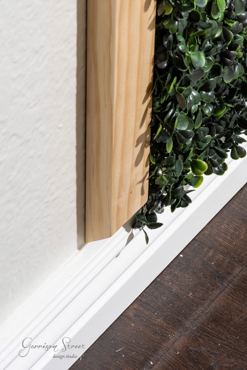 Close-up of wooden paneling with a green wall behind it, set against a white wall and a dark hardwood floor. The design studio's logo is visible in the lower left corner.