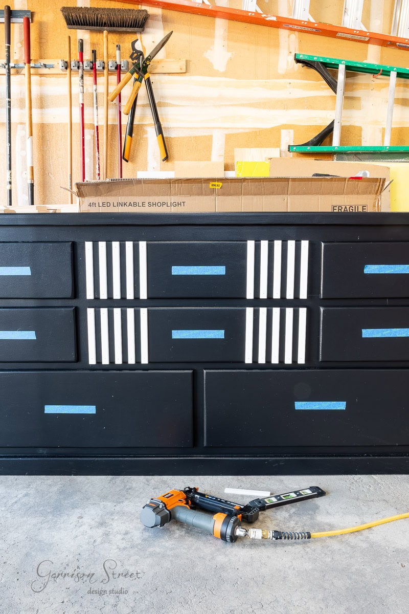In the workshop scene, a black cabinet with white stripes and blue tape stands ready. Nearby, a nail gun with an air hose lies on the floor, surrounded by tools like ladders and brooms, while a box labeled "LED linkable shoplight" sits on a shelf above.