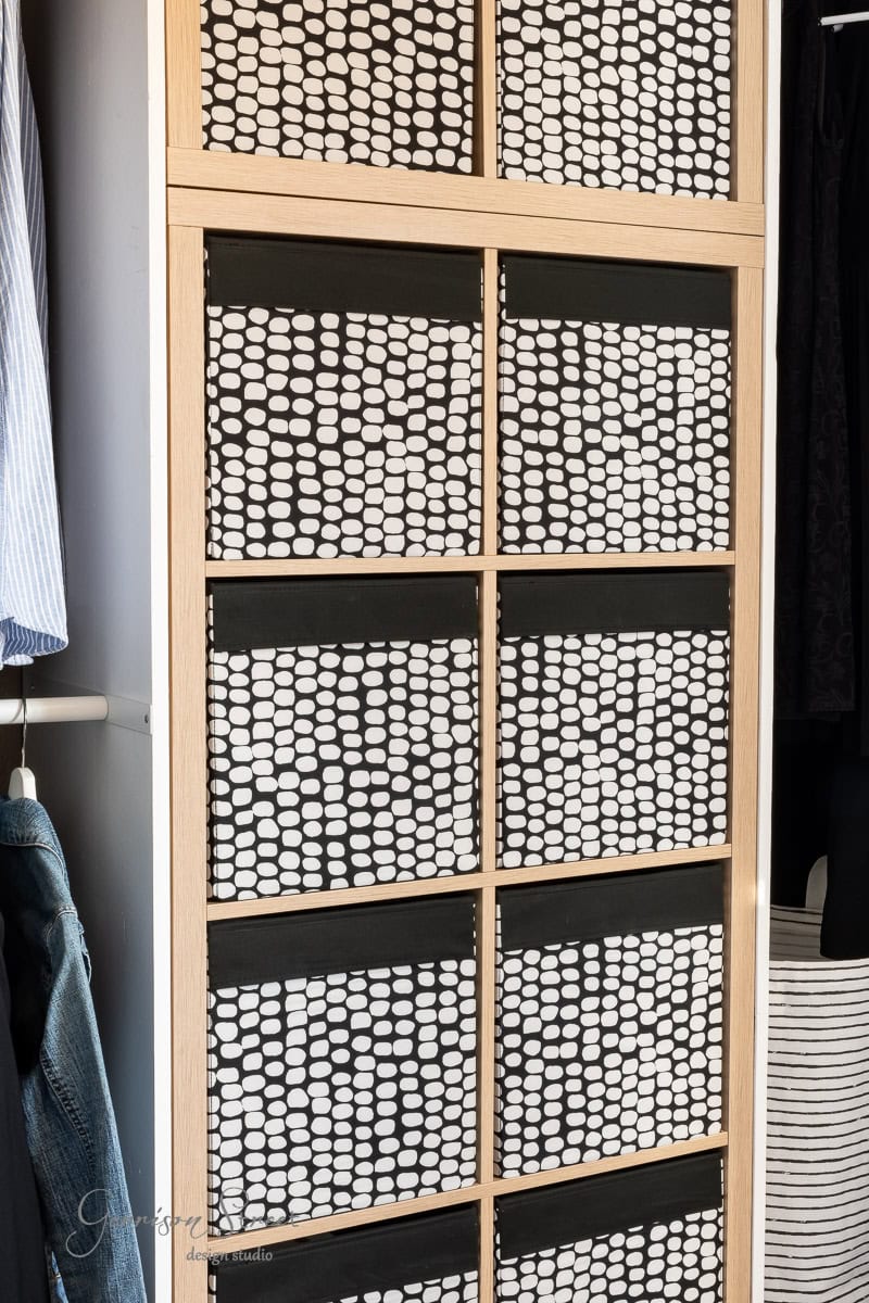 A closet makeover showcases sliding doors with a black and white geometric pattern. The stylish update reveals clothing inside, like a blue striped shirt and denim fabric, all framed by light wood for that perfect DIY touch.