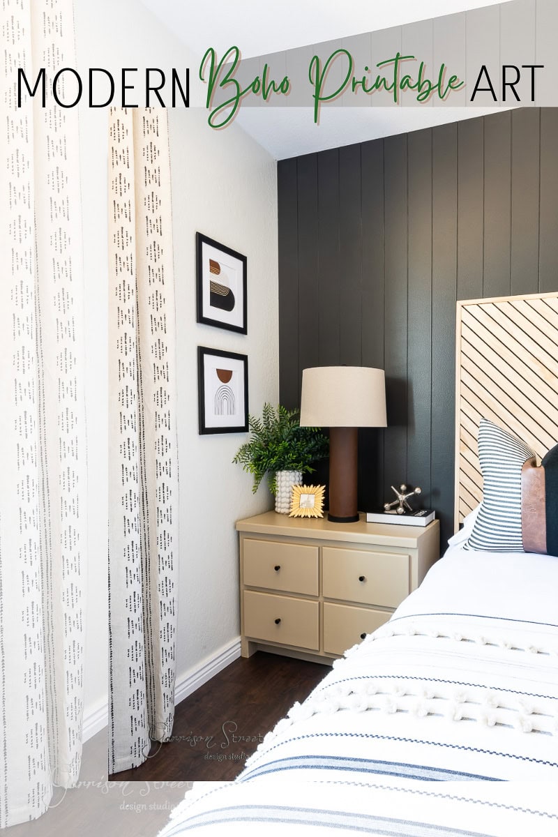 A modern bedroom with a black accent wall, beige dresser, and decorative lamps features printable boho art. Framed pieces are displayed above the dresser, and patterned curtains hang by the window. The bed showcases striped bedding with a boho style, titled "Modern Boho Printable Art.