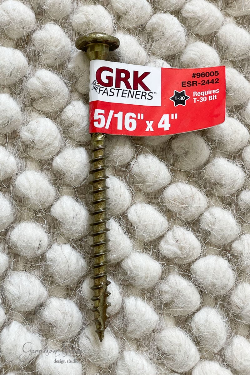 A 5/16" x 4" GRK fastener with a red and white label rests on a textured white surface. The label confirms it requires a T-30 bit.