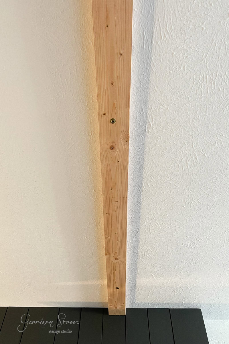A wooden plank is vertically attached to a textured white wall. The image captures a partial view of a dark-colored deck at the bottom, with "Garrison Street design studio" elegantly inscribed in the lower left corner.