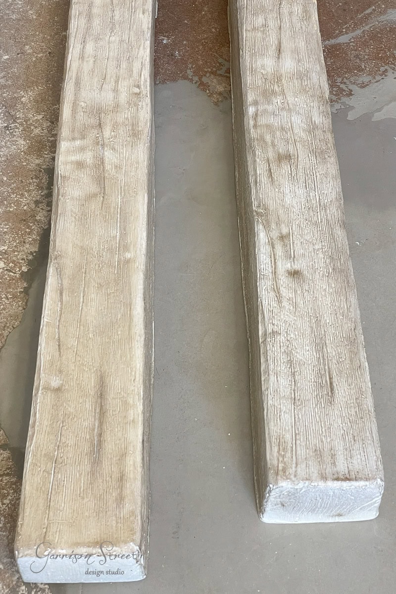 Two wooden beams with a light, natural finish rest on a textured concrete floor. The surface shows a visible grain pattern. A logo in the bottom left corner reads "Garrison Street Design Studio."