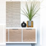 A modern makeover of the IKEA Kallax white cabinet with fluted wooden doors stands against a textured wall. On top, there's a tall plant in a gray pot and a round black vase. Text reads "DIY IKEA Kallax Hack Makeover with Fluted Doors, Garrison Street Design Studio.