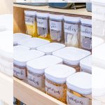 Well-organized pantry drawer with labeled containers holding pasta, rice, noodles, cookies, snacks, popcorn, and quinoa. White lids and clear containers show the contents inside. Text overlay reads "DIY Pantry Organization for Deep Kitchen Cabinets.